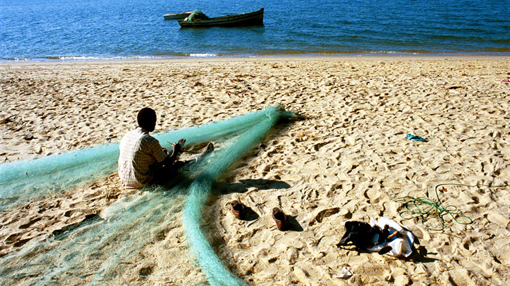 A fisherman repairing his nets on a beach in Mozambique